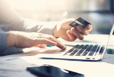 Mann sitzt vor dem Laptop und hält eine Kreditkarte in der Hand